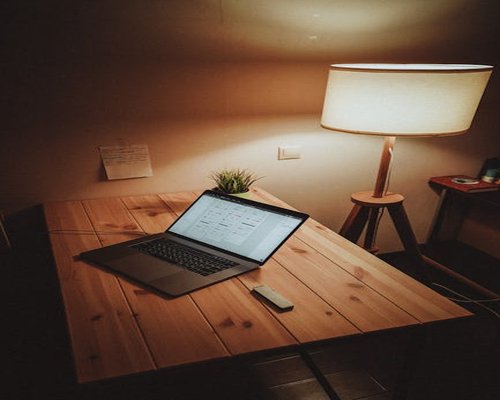 A well lit home office setup with a warm desk lamp beside a laptop